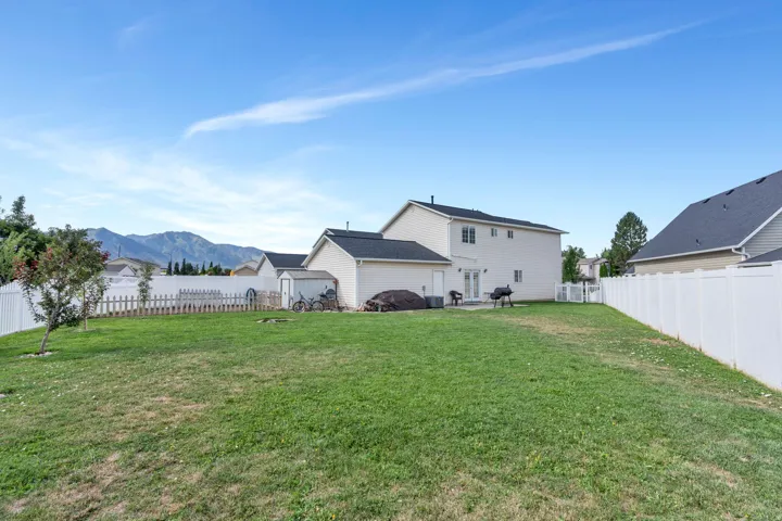 Expansive grassy yard with mountain backdrop, white vinyl perimeter fencing, and a patio area