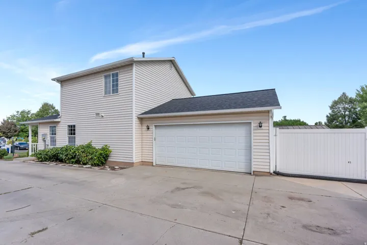 Two-story exterior with light-colored siding, attached two-car garage, and a white privacy fence