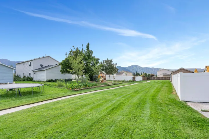 Expansive manicured lawn with a concrete pathway, privacy fencing, mature trees, and mountain scenery
