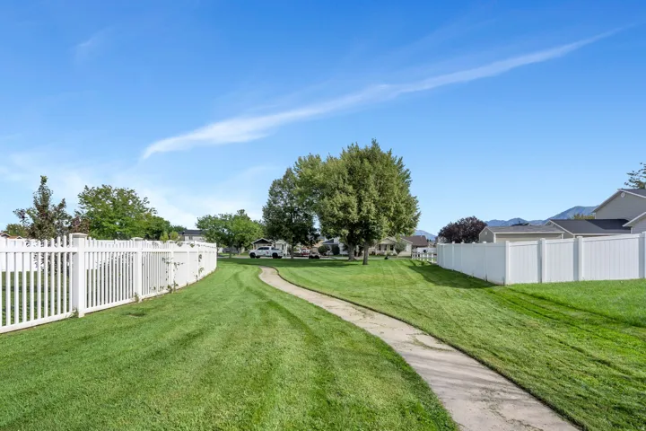 Expansive green space featuring a winding paved path, mature trees, and white privacy fencing
