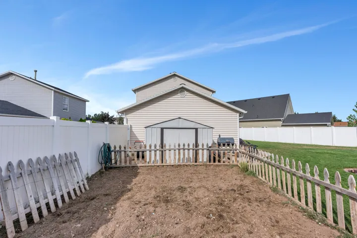 Fenced backyard featuring a cultivated garden area, white privacy fencing, and an additional storage shed