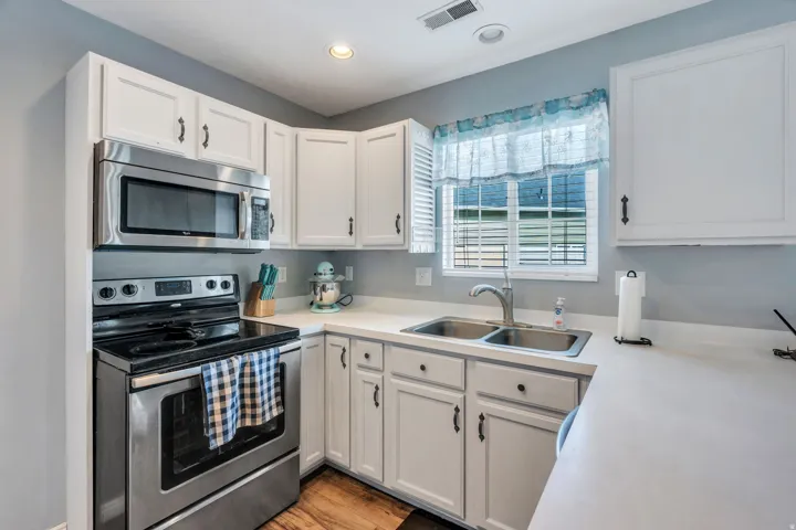 White cabinetry, stainless steel appliances, solid surface countertops, dual basin sink, and wood-finish flooring