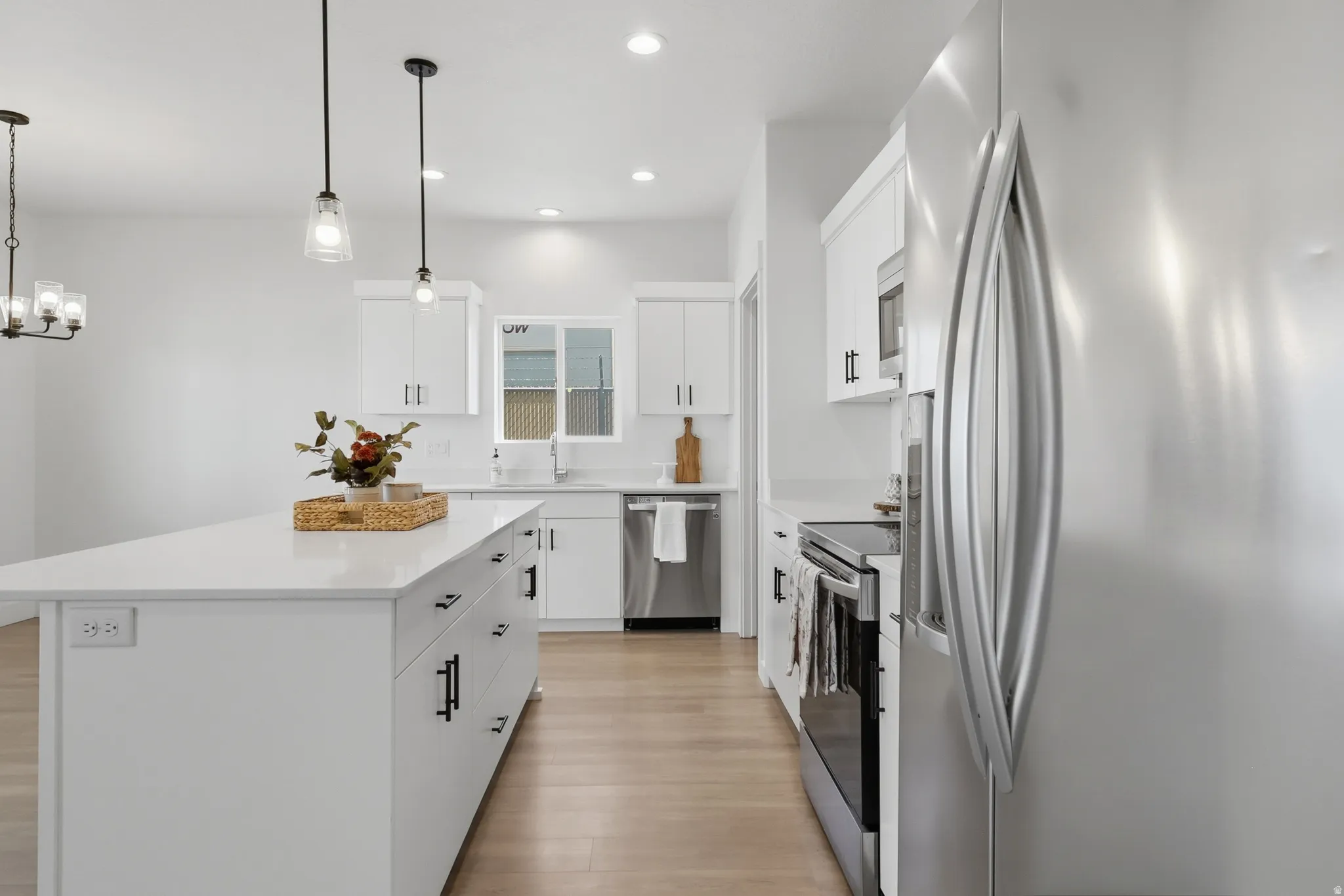 Kitchen featuring a large center island with white countertop, white cabinetry with dark hardware, stainless steel appliances, and wood-finish flooring