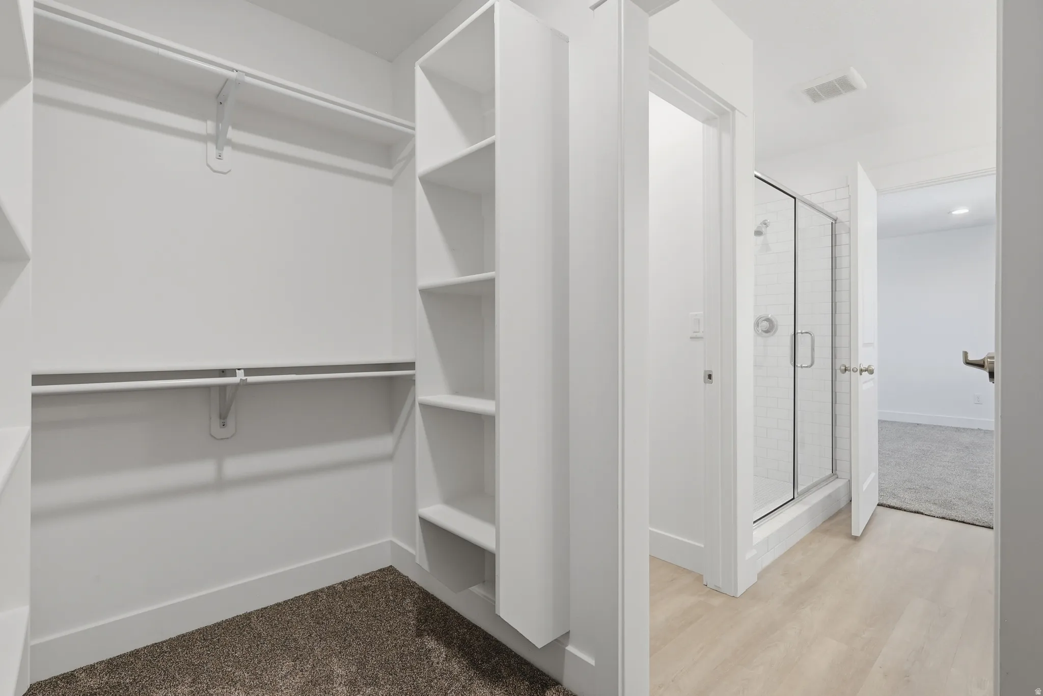 Built-in shelving, hanging rods, framed glass shower, white subway tile, and light wood-finish flooring
