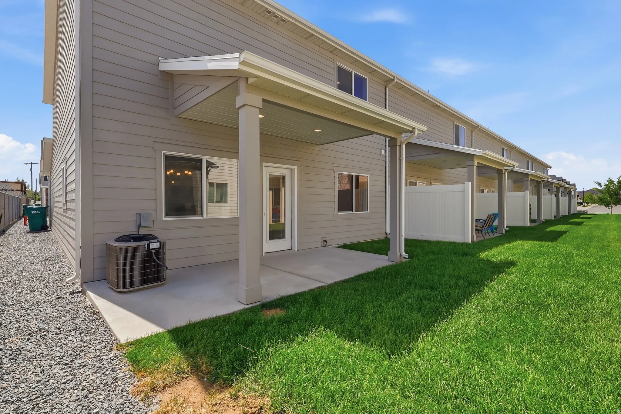 Rear exterior featuring covered patios, concrete pads, green lawn, and gravel landscaping