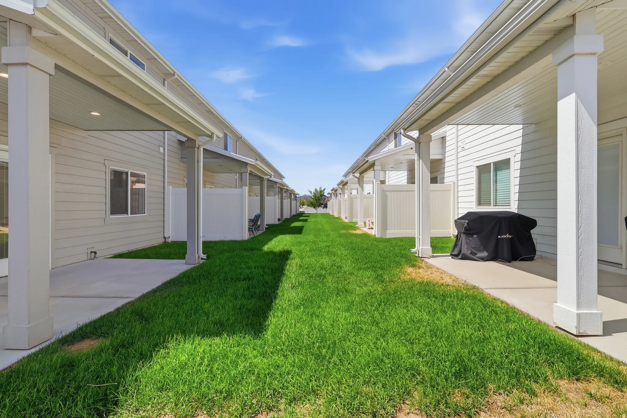Covered concrete patio, white vinyl siding, white privacy fencing, and green lawn space