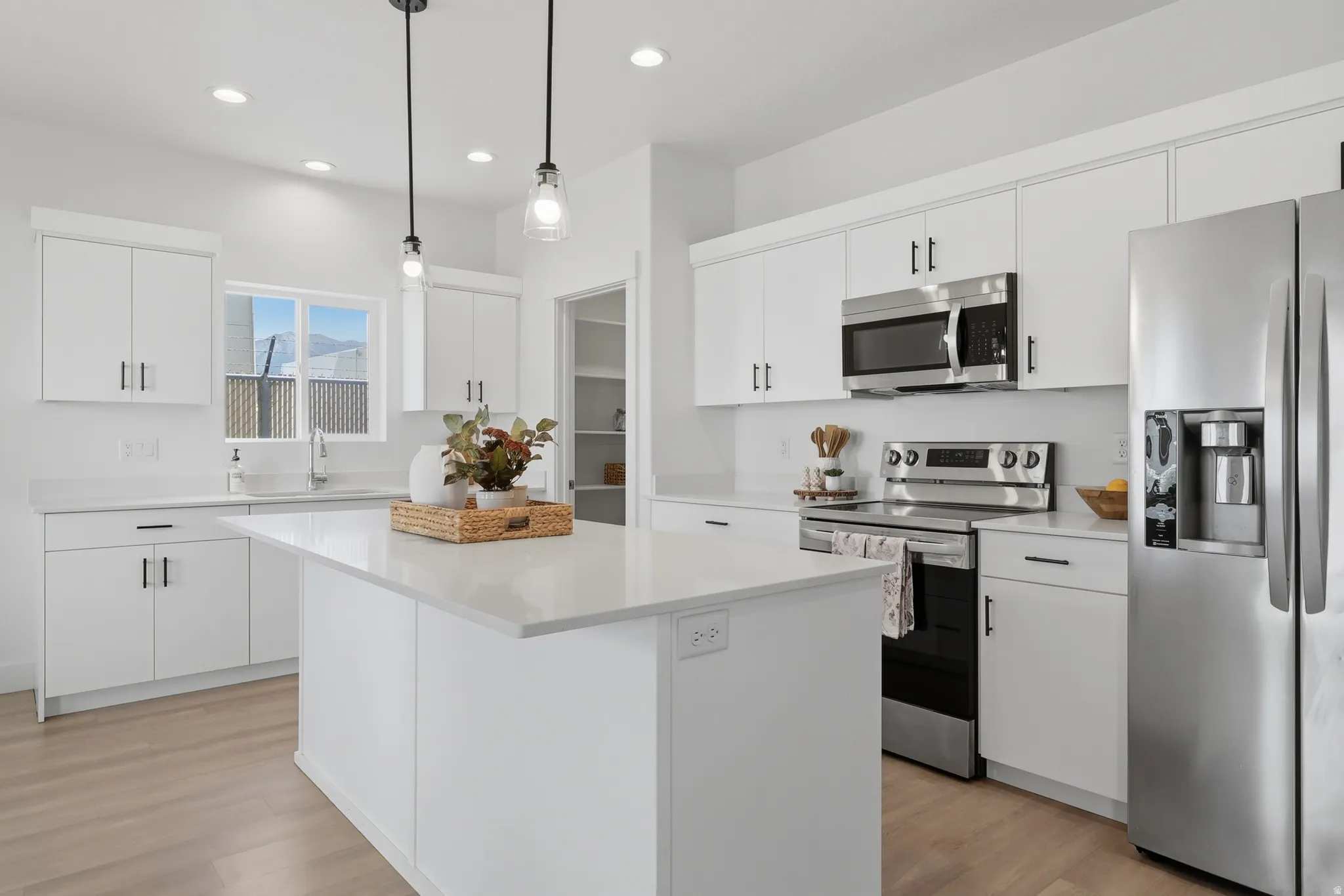 Bright kitchen featuring a central island, white cabinetry with dark hardware, stainless steel appliances, and light wood-finish flooring