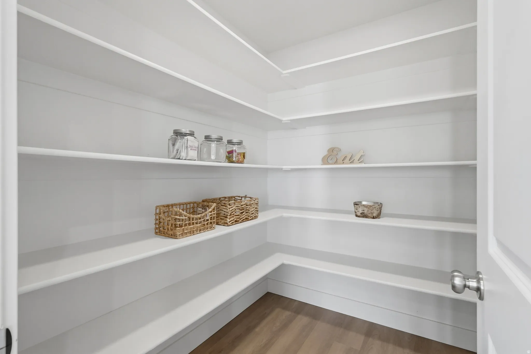Spacious pantry with multiple white shelves and wood-finish flooring