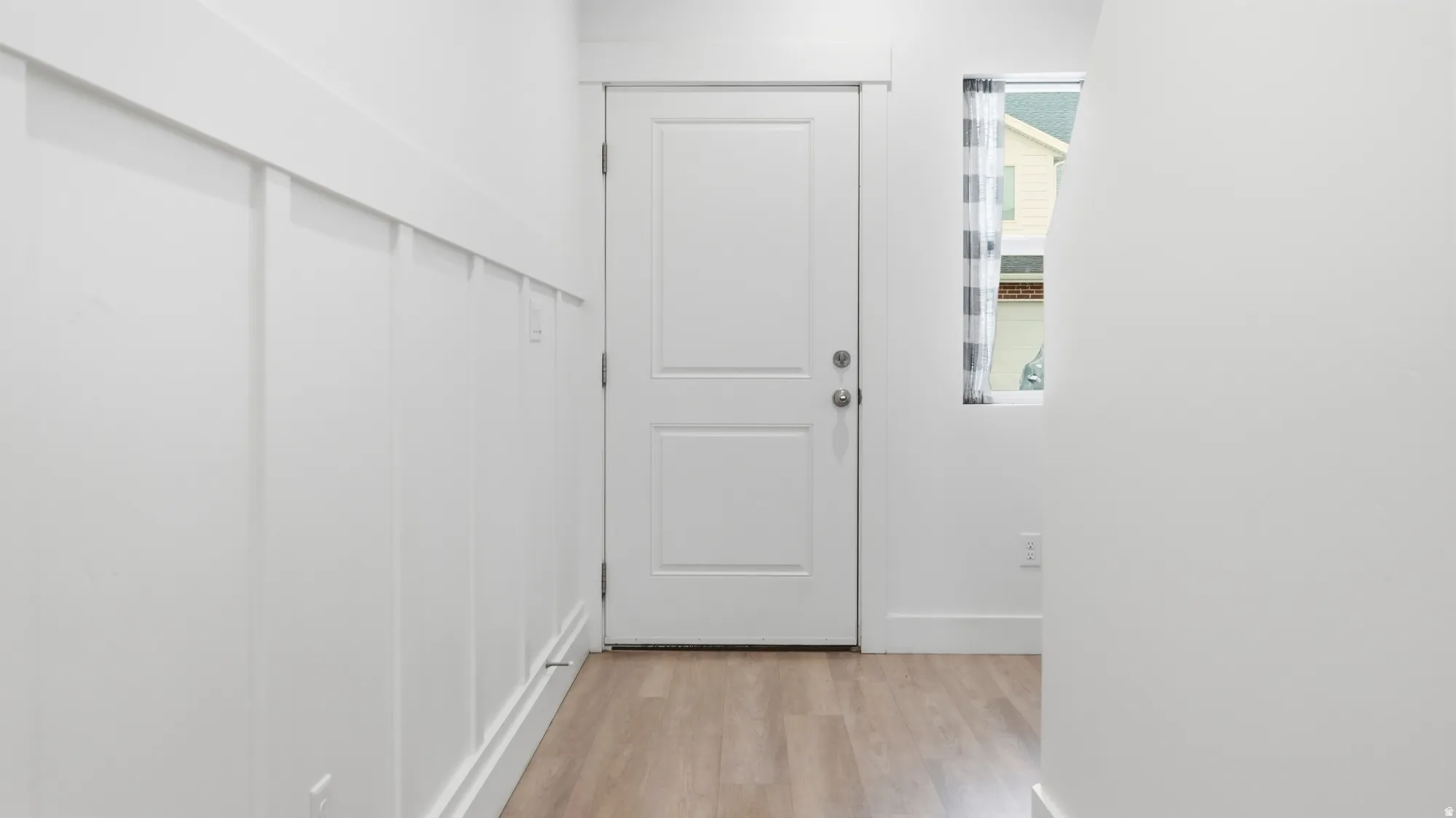White paneled accent wall, wood-finish flooring, white painted door, and recessed lighting