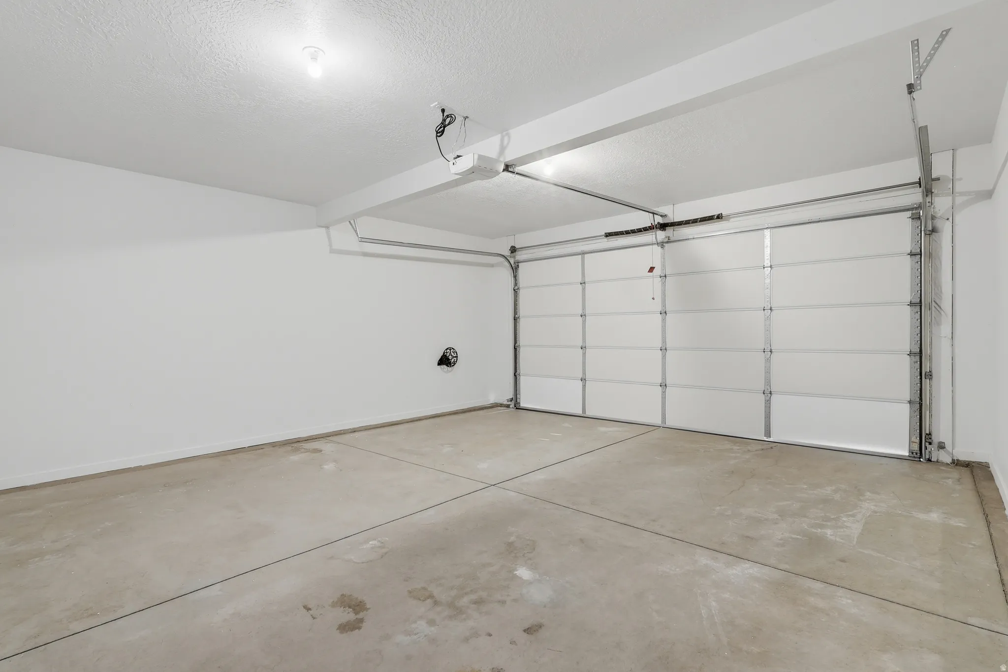 Concrete floor, white walls, overhead lighting, garage door opener, panel garage door