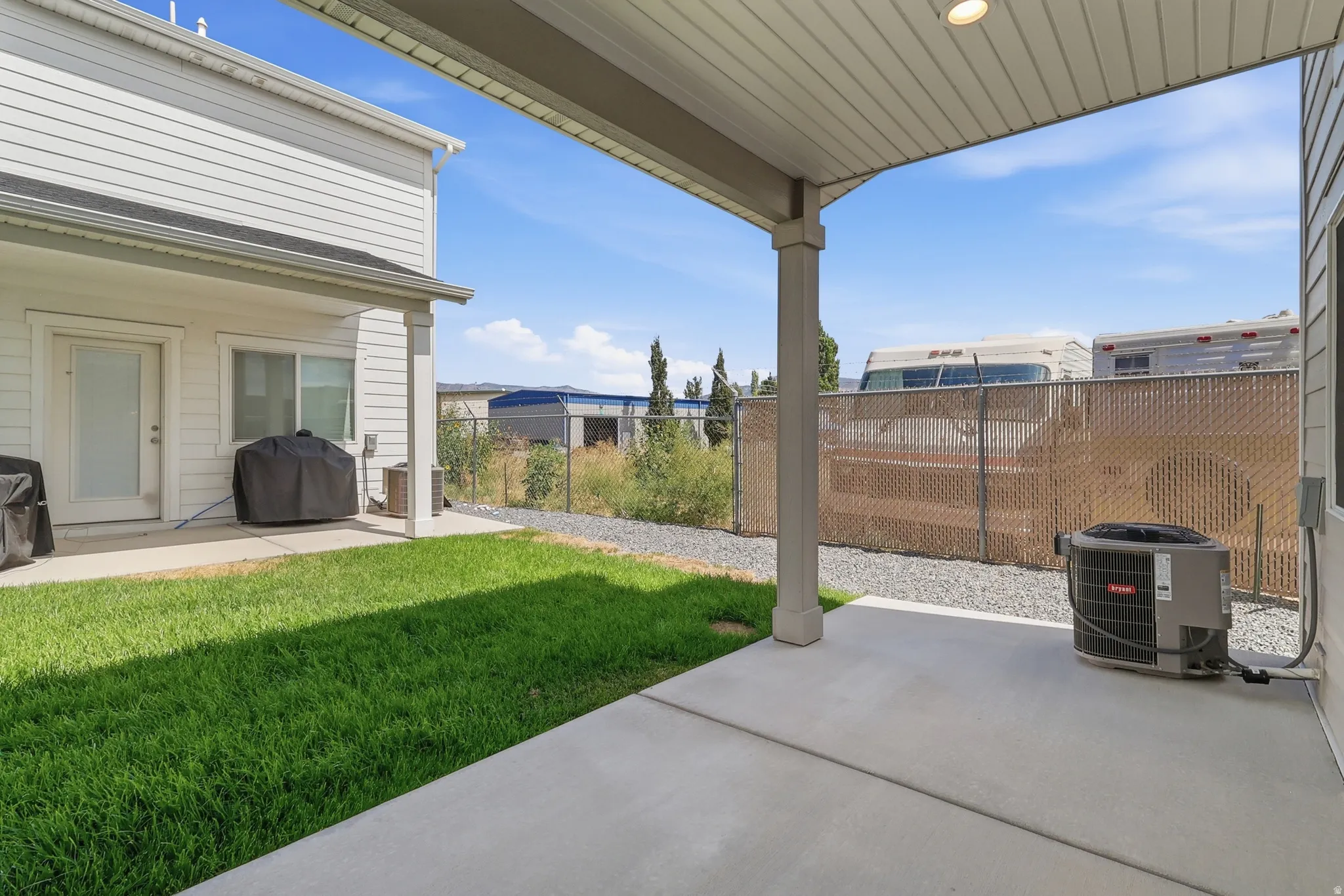 Concrete patio with an overhead cover, a privacy-screened chain-link fence, and a grassy area