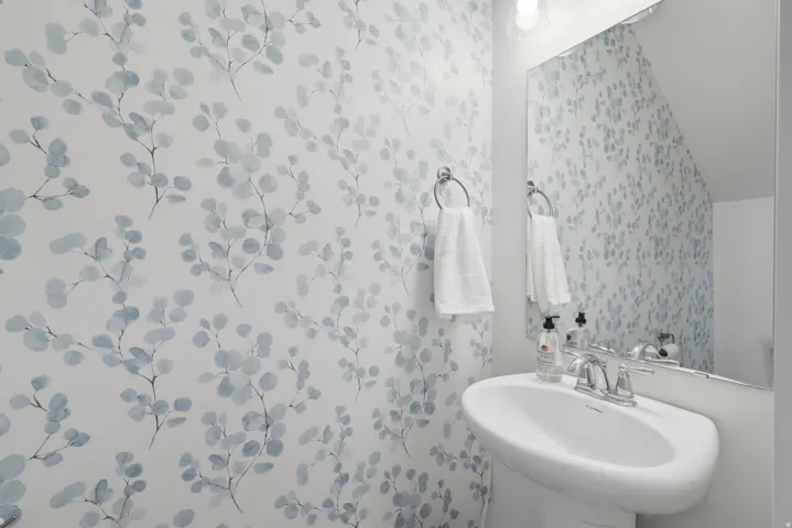 Pedestal sink with chrome fixtures and an oval mirror, complemented by botanical-patterned wallpaper