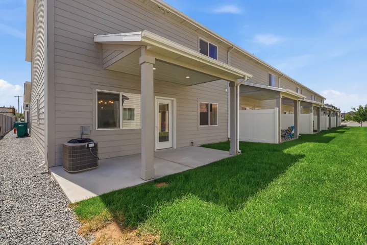 Rear exterior featuring covered patios, concrete pads, green lawn, and gravel landscaping