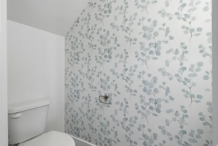 White toilet with a patterned accent wall and a wall-mounted towel holder