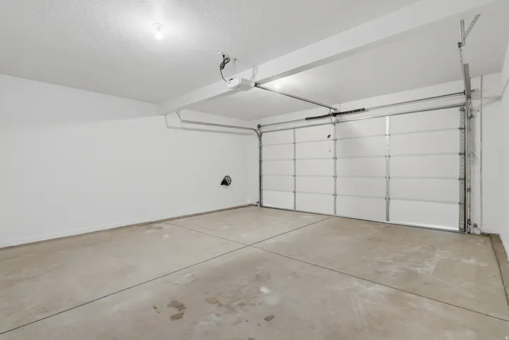 Concrete floor, white walls, overhead lighting, garage door opener, panel garage door