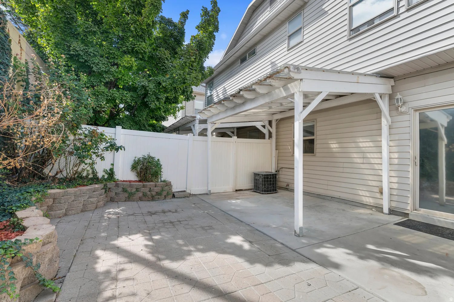 Paved patio featuring a white pergola structure and a privacy fence