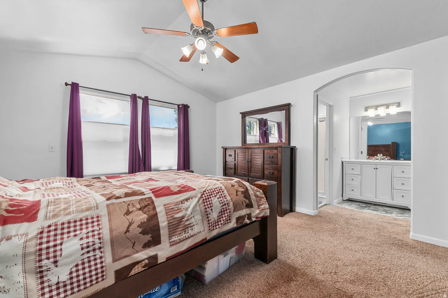 Vaulted ceiling with a ceiling fan, three windows, and carpet flooring