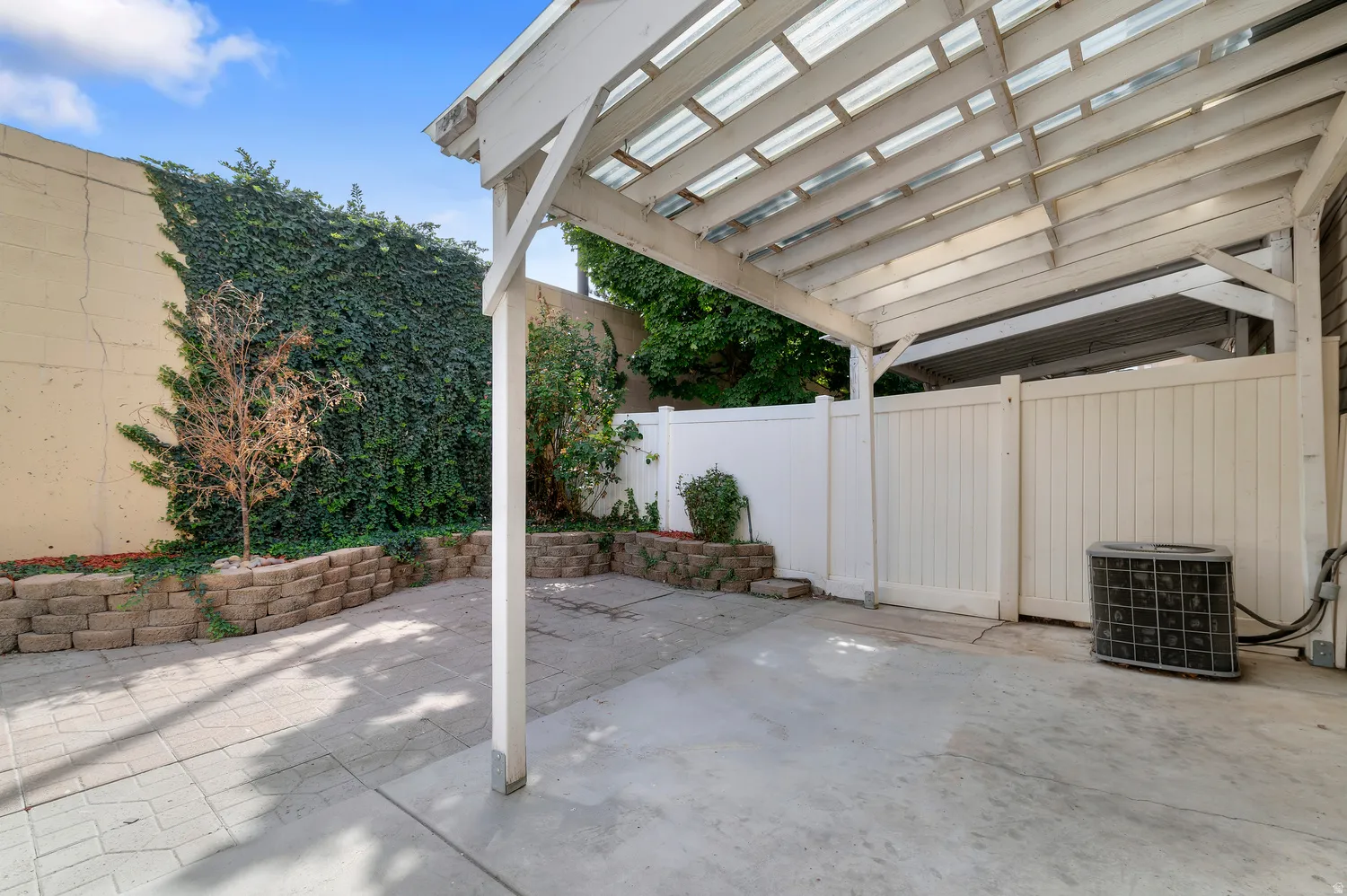 Paved patio area featuring a white wood pergola with a translucent roof, and a privacy fence