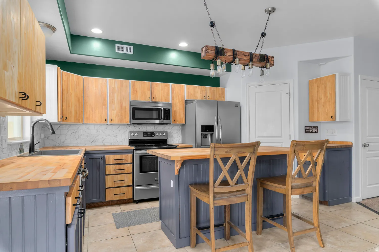 Kitchen featuring wood countertops, stainless steel appliances, a tile backsplash, recessed lighting, and a kitchen island with seating