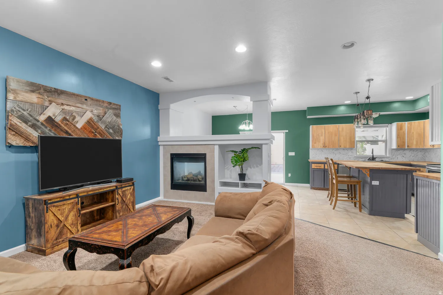 Integrated living space featuring a built-in fireplace, carpeted flooring, recessed lighting, and a kitchen with wood-finish upper cabinetry and a breakfast bar island