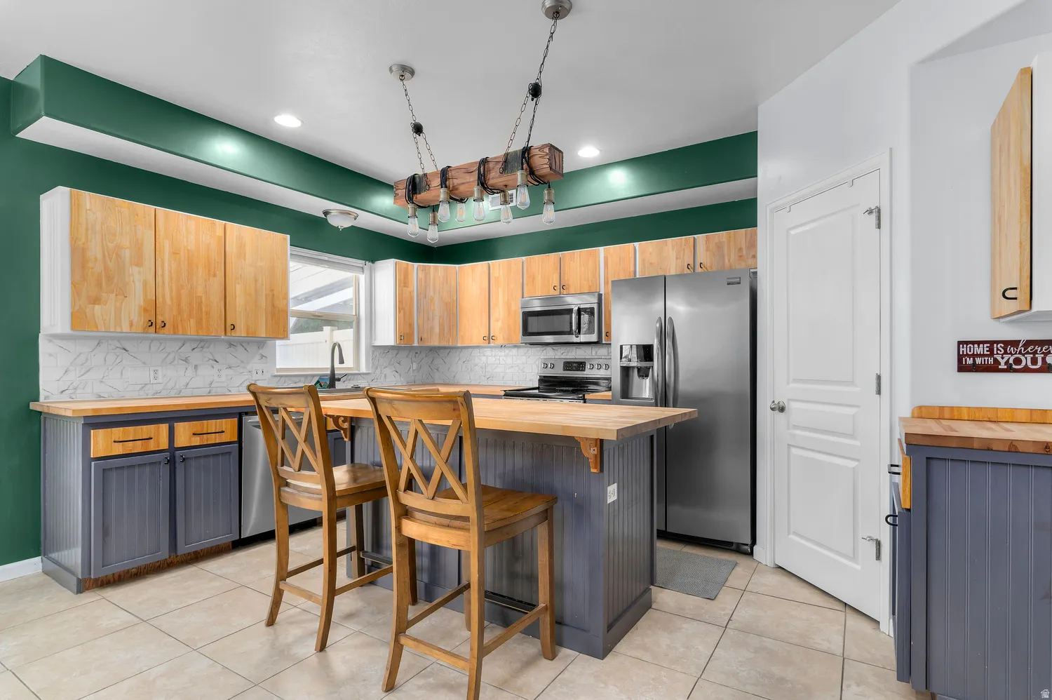 Kitchen featuring wood-finish cabinetry, stainless steel appliances, a wood-finish island, and tile flooring