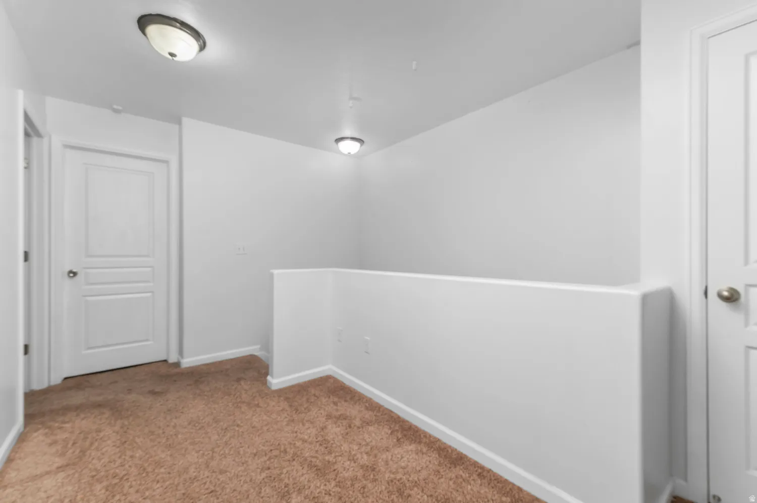 Open loft area with neutral-toned carpeting, white walls, and two-panel interior doors