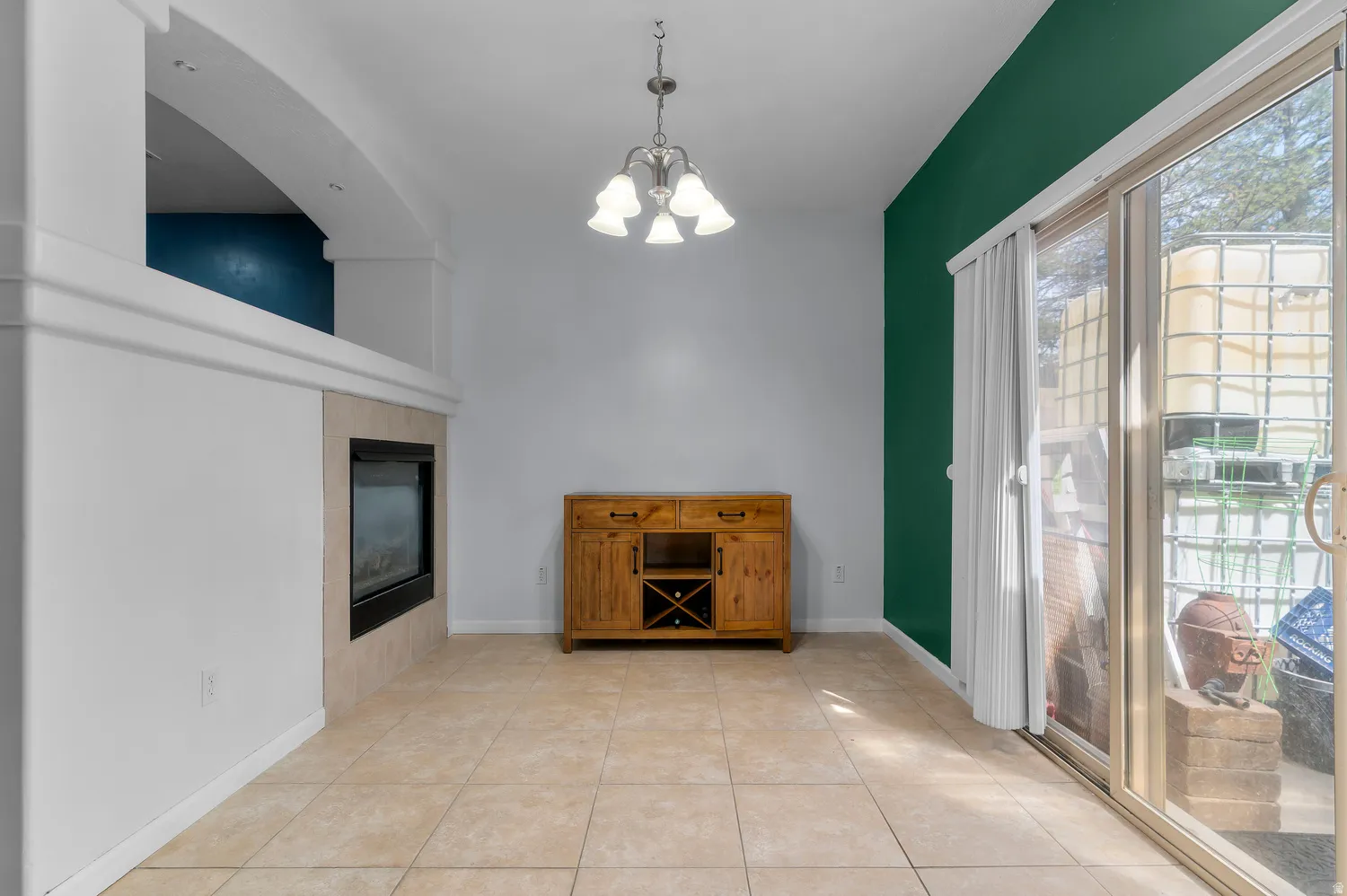 Recessed fireplace with a tile surround, arched architectural detail, sliding glass door, and a traditional chandelier