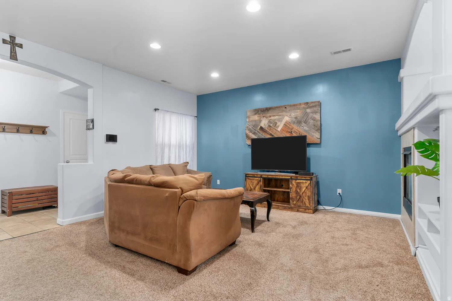 Spacious recreation room featuring a striking blue accent wall, recessed ceiling lighting, neutral carpet flooring, and built-in entertainment cabinetry with wood-finish details
