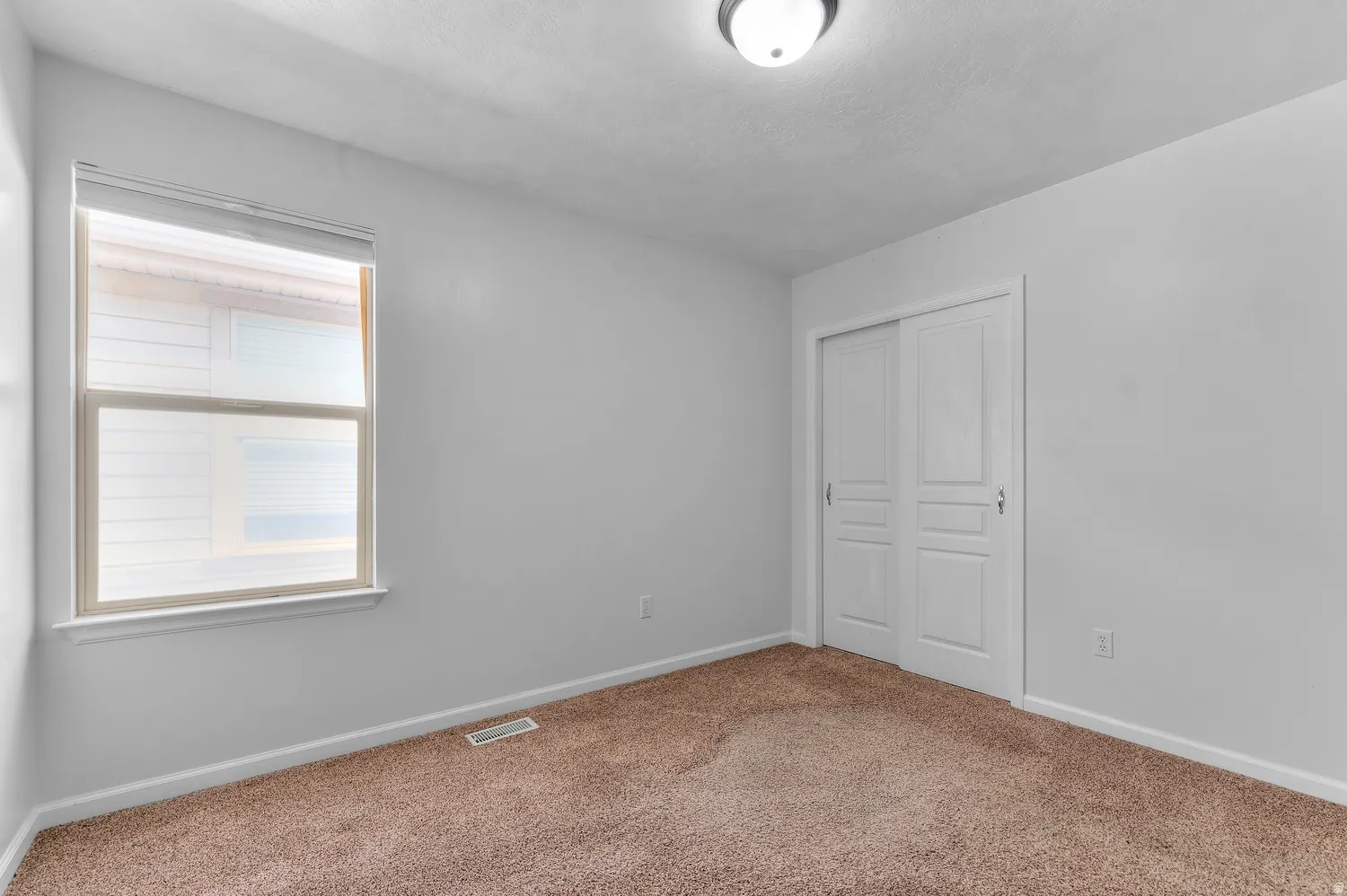 Neutral wall paint, brown carpet flooring, and a single window with blinds