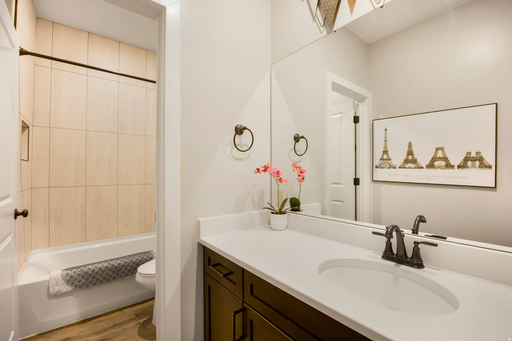 Bathroom featuring a single vanity with a white countertop, dark wood-finish cabinetry, an undermount sink, and a black faucet