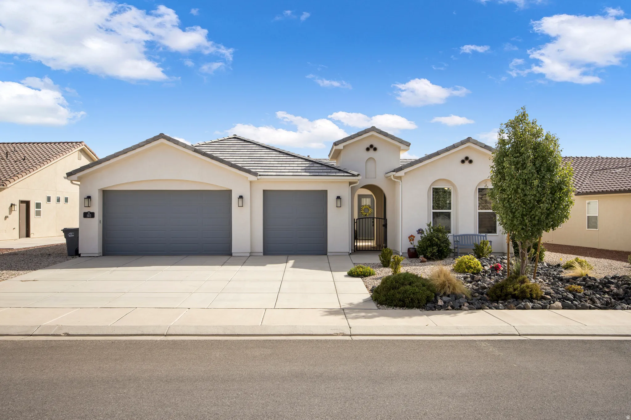 Stucco exterior with a tiled roof, two-car garage, arched entry, and xeriscaped front yard