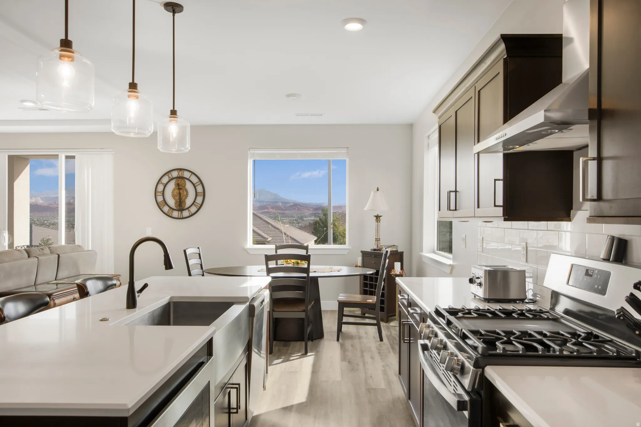 Kitchen featuring a stainless steel range, white subway tile backsplash, dark wood-finish cabinetry, and an island with a farmhouse sink and pendant lighting