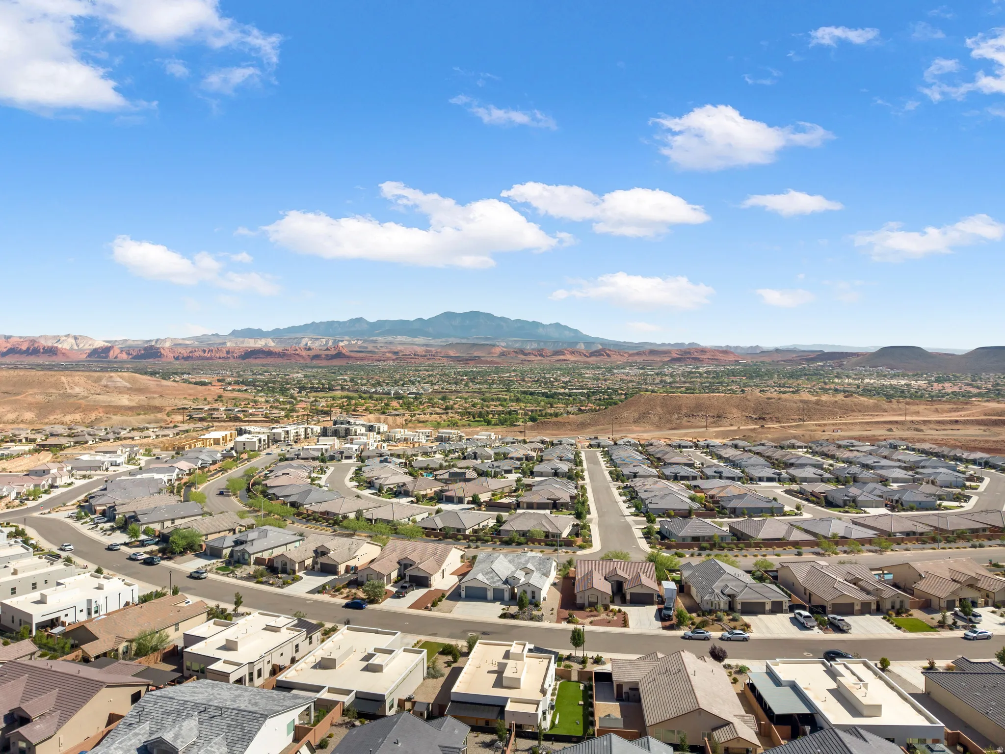 Expansive residential community with diverse roofing styles, set against a backdrop of distant mountains and desert terrain
