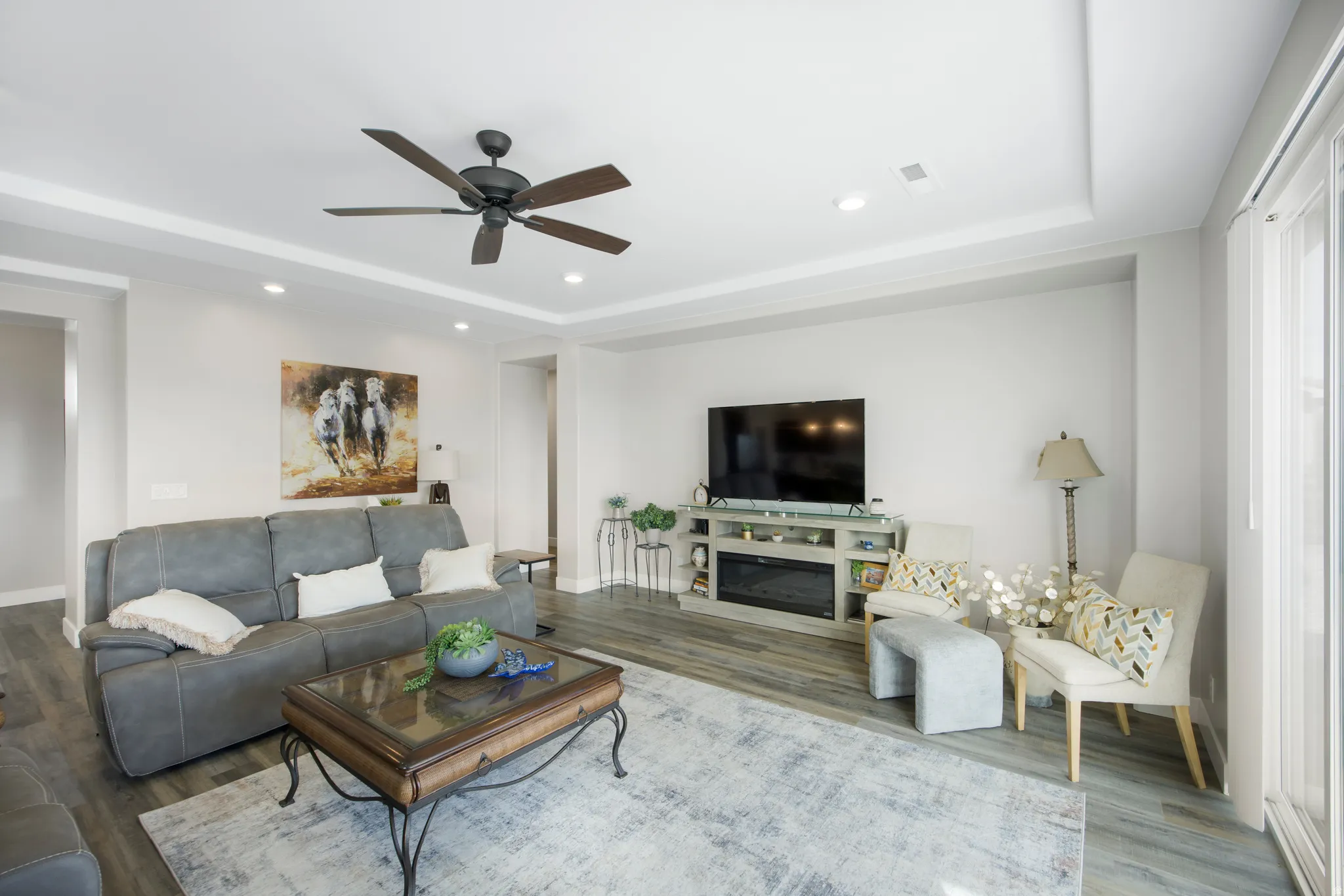 Recessed lighting, tray ceiling, ceiling fan, wood-finish flooring, and built-in electric fireplace