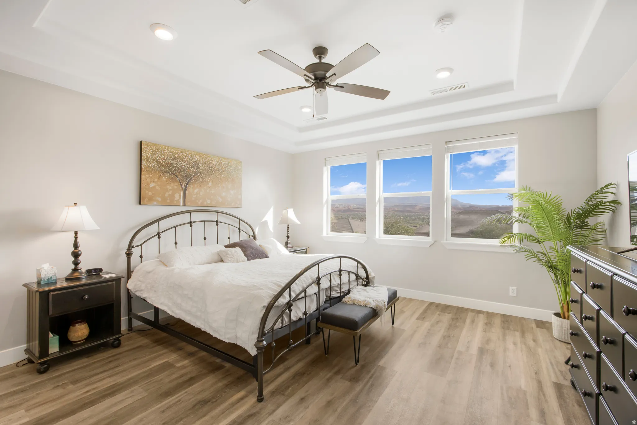 Tray ceiling with recessed lighting and a ceiling fan, three large windows, and wood-finish flooring