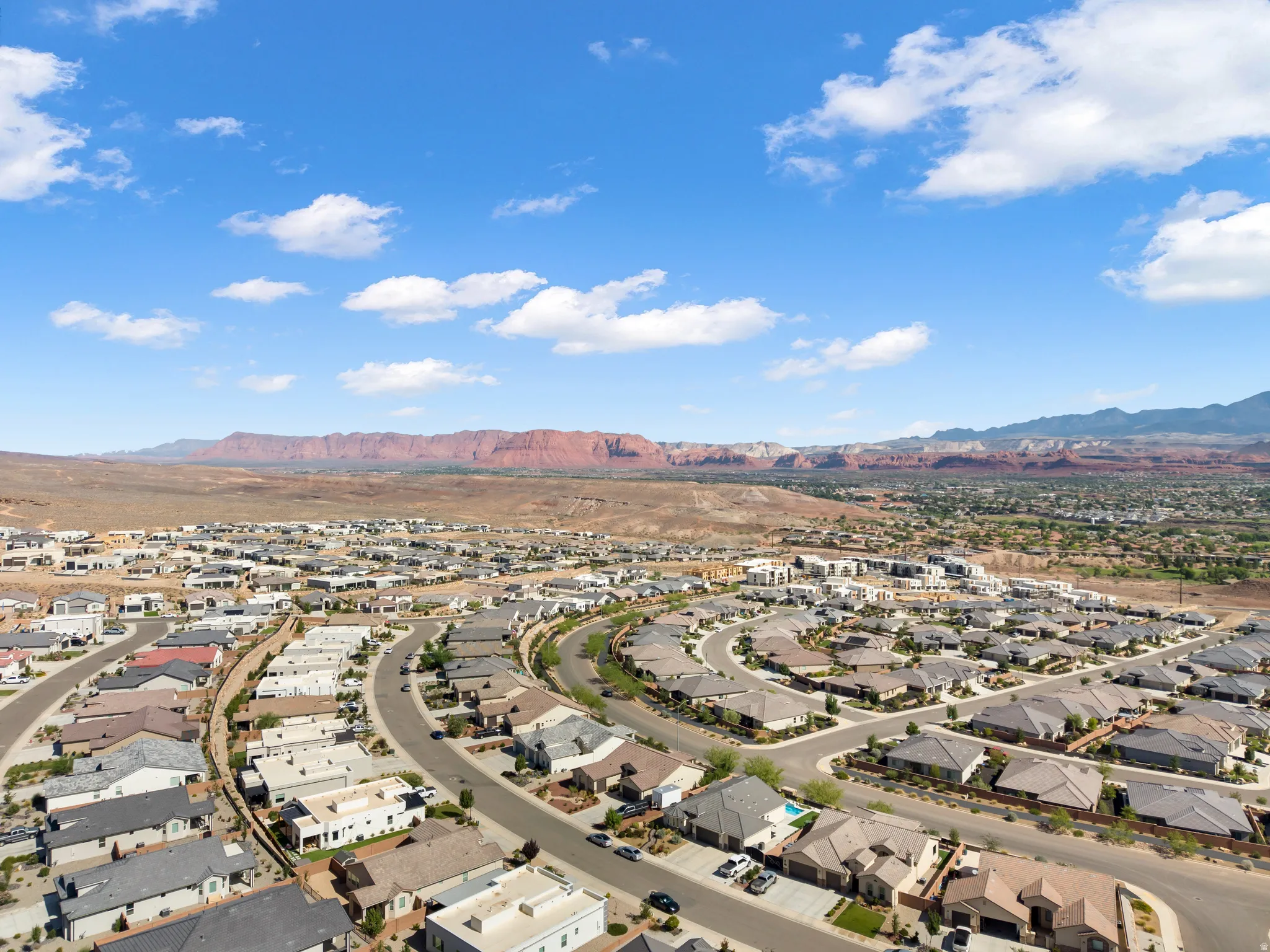 Expansive community with varied architectural styles, curved street layouts, and red rock formations