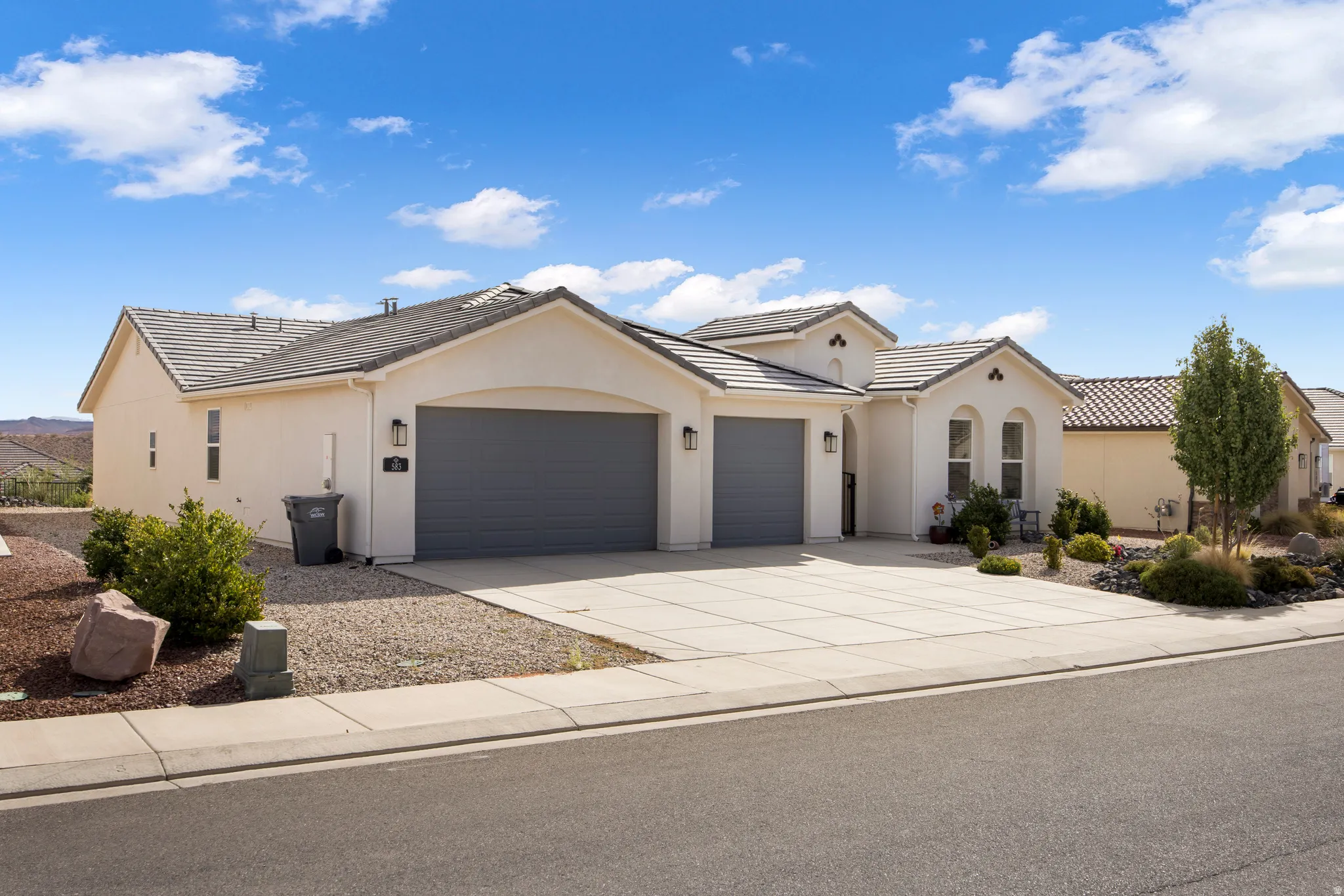 Stucco exterior with a tiled roof, featuring a concrete driveway, two garage doors, and xeriscaped landscaping