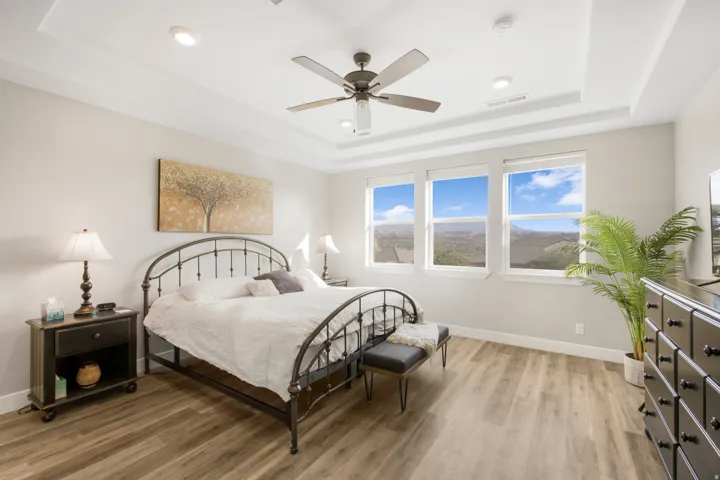Tray ceiling with recessed lighting and a ceiling fan, three large windows, and wood-finish flooring