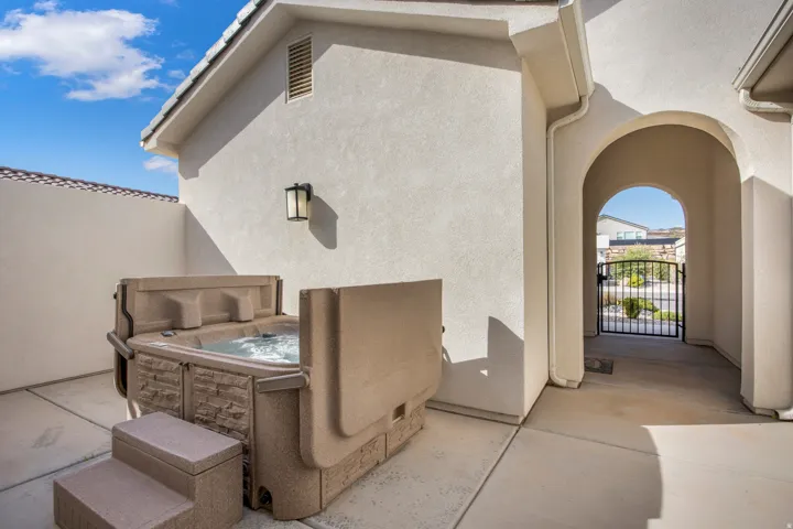 Private enclosed courtyard featuring a hot tub, concrete patio, stucco walls, and an arched entryway leading to a wrought iron gate