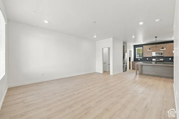 Open-concept interior featuring light-toned wood-finish flooring, recessed lighting, and kitchen cabinetry with a minimalist flat-panel design