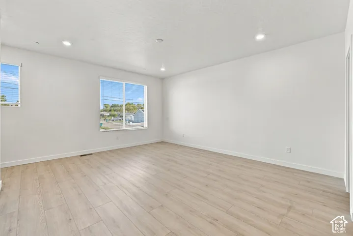 Neutral-toned room featuring wood-finish flooring, recessed lighting, and large windows with horizontal blinds