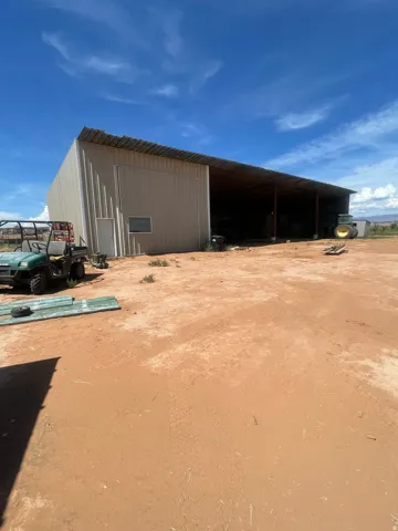 Metal-sided outbuilding with a corrugated roof, featuring a covered open-sided extension and a side entry door