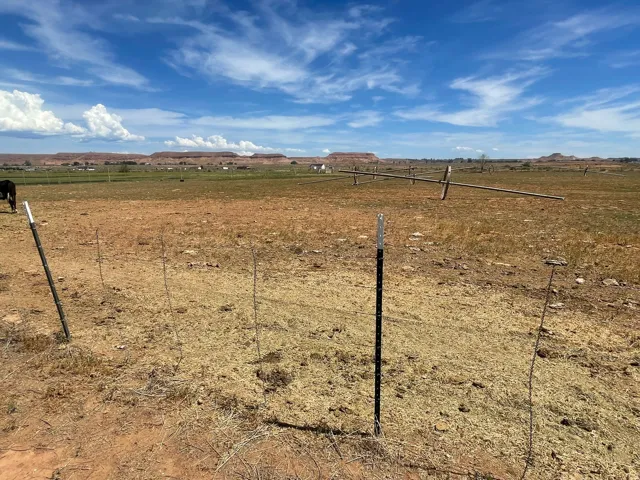 Expansive open land with distant red rock formations and a partially visible fence line