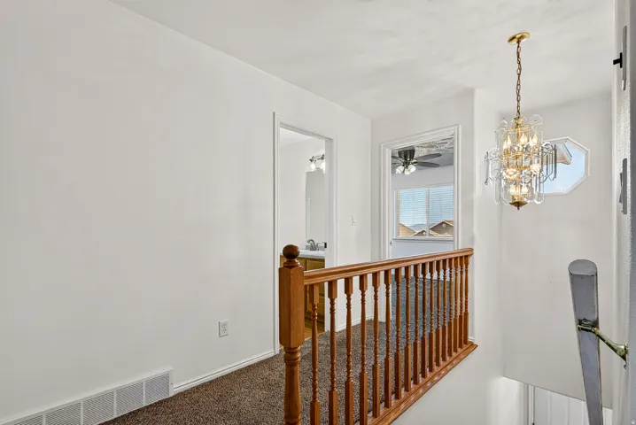 Staircase with wood balusters, carpeted landing, and overhead chandelier