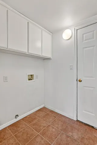 White cabinetry with shaker-style doors, tile flooring, and wall-mounted lighting