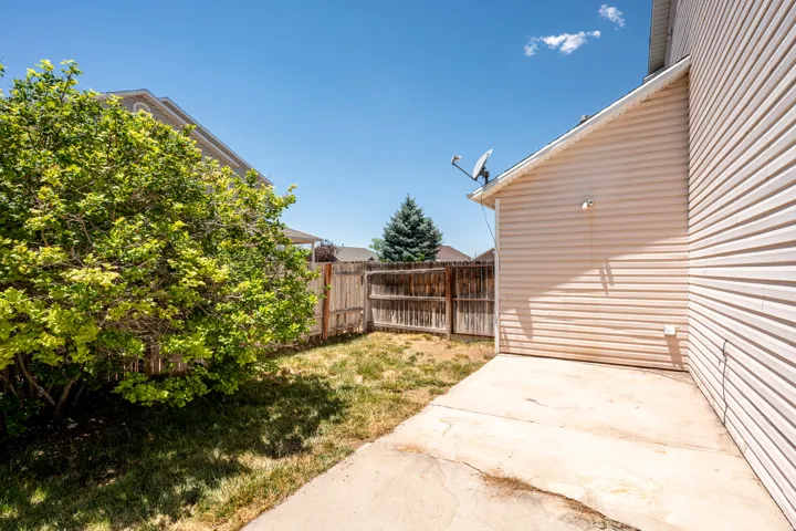 Rear yard featuring a concrete patio, wood fence, and mature shrubbery