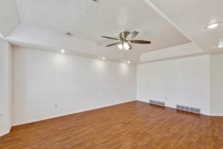 Spacious room featuring wood-finish flooring, a tray ceiling, recessed lighting, and a ceiling fan with light