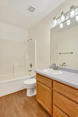 Wood-finish flooring, full bathtub with shower, wood-finish vanity with countertop, and overhead lighting