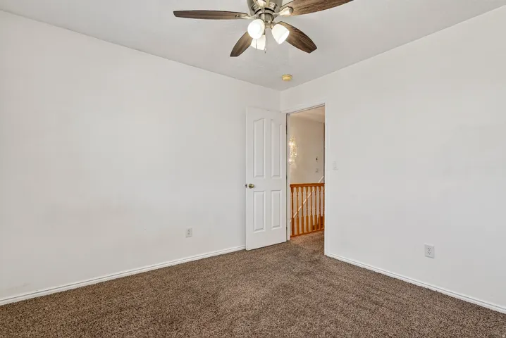 Carpeted room with a ceiling fan, white walls, and a paneled door