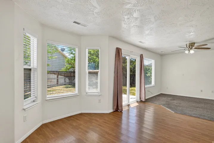 Wood-finish flooring, multiple windows with blinds, sliding glass door, ceiling fan with integrated lighting, and carpeted area
